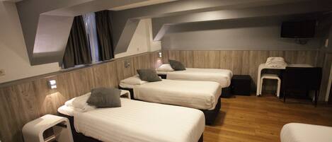 A hotel room with three single beds, a small desk, a chair, and a TV mounted on the wall.