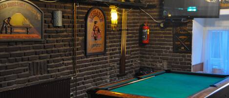 A billiards table in a room with brick walls, a mounted television, and a fire extinguisher.