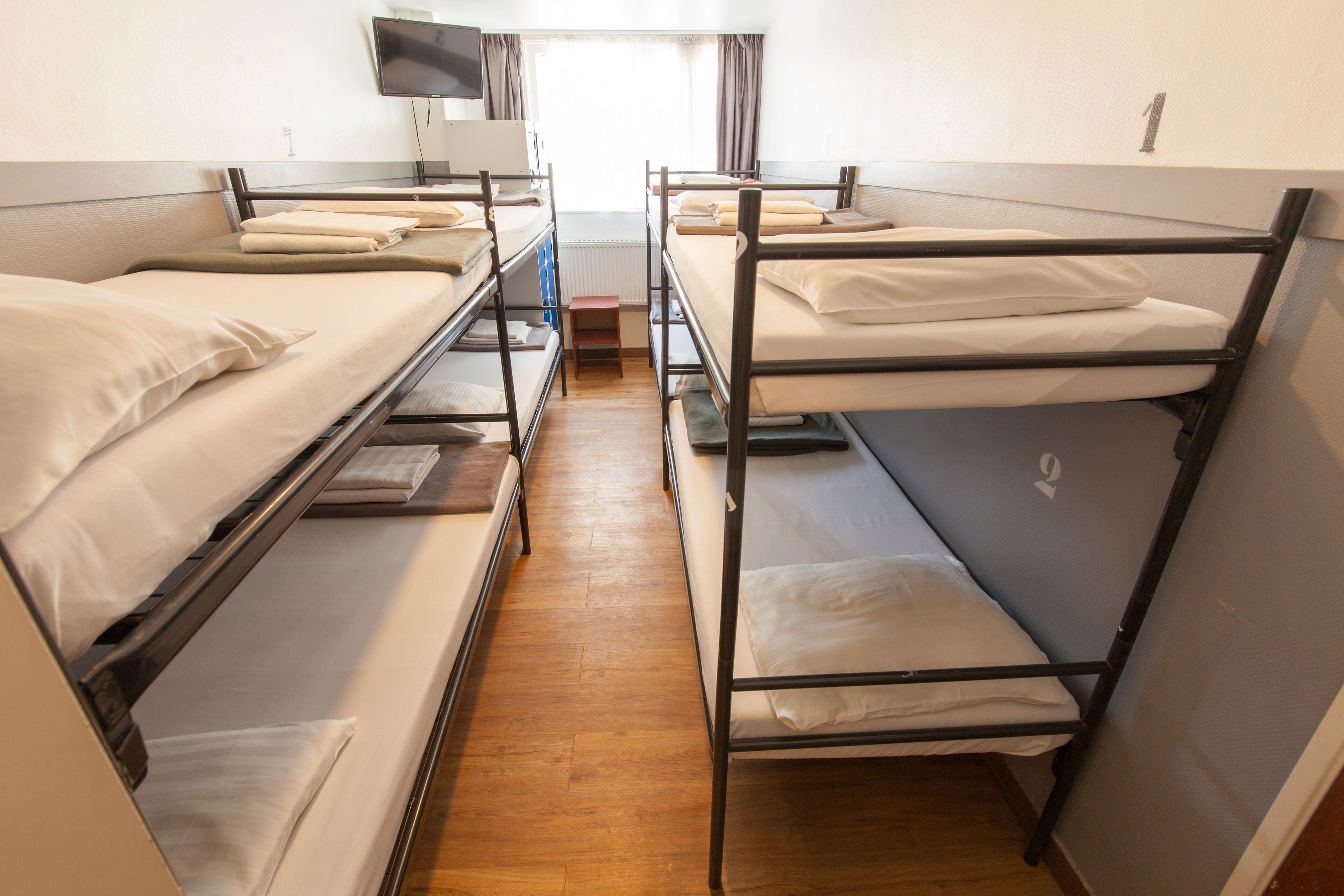 A dormitory room with bunk beds, a television, and a window with curtains.
