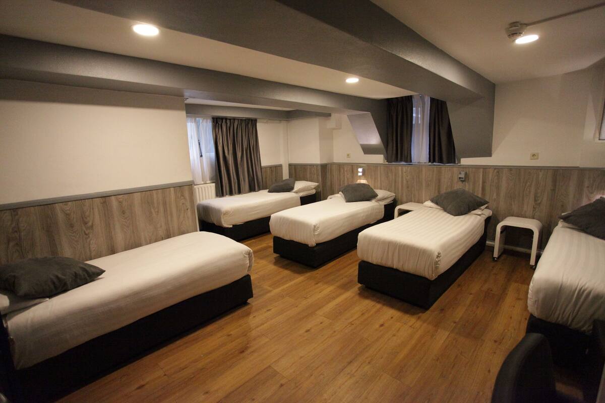 Una habitación con cuatro camas individuales dispuestas en forma de U, suelo de madera y una pequeña mesa.