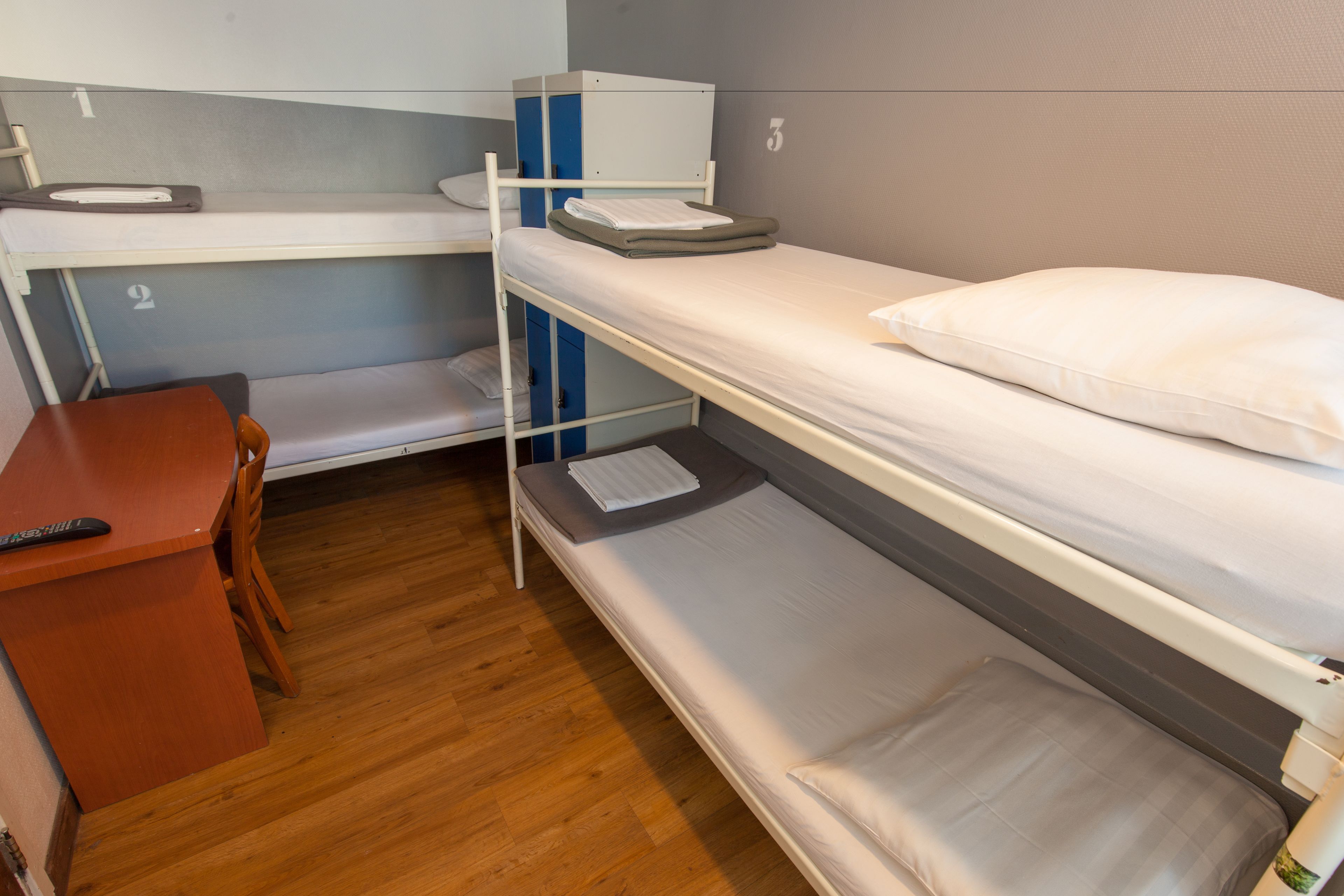 Habitación con literas, un escritorio, una silla, suelo de madera y almohada blanca en la camastro superior.