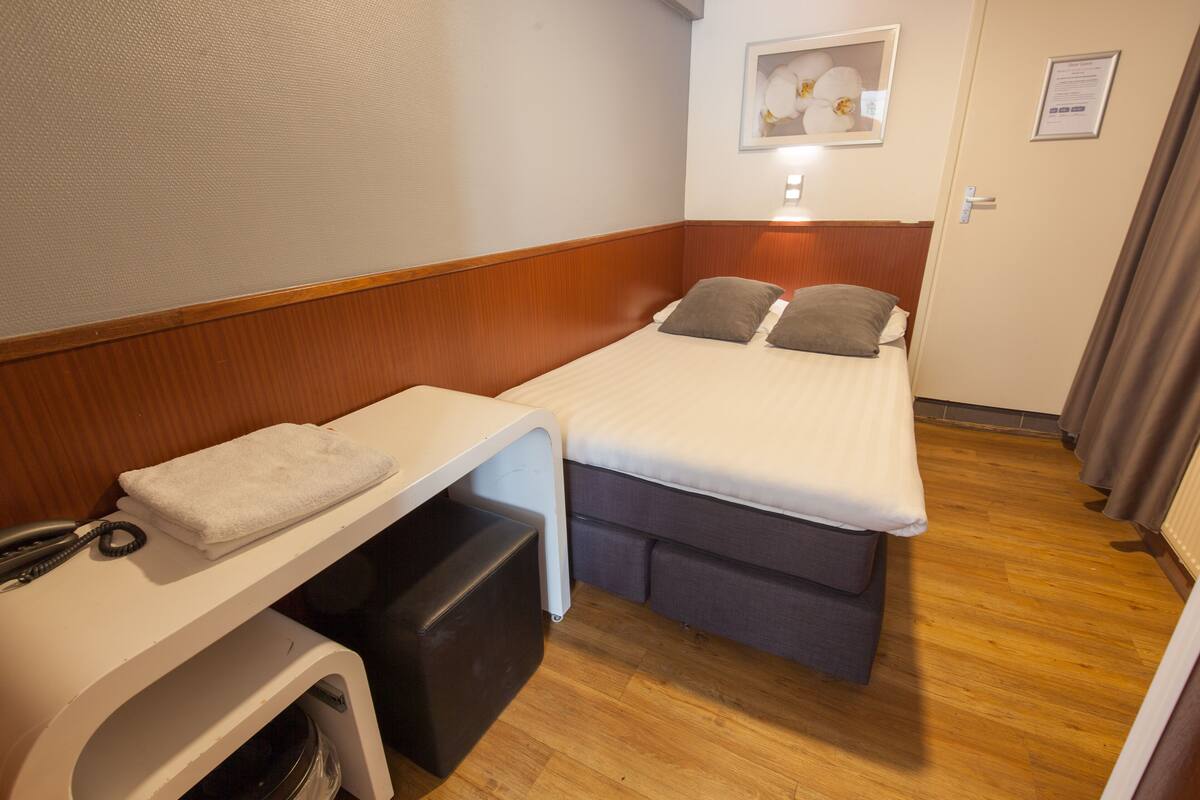 Habitación de hotel pequeña con una cama individual, un escritorio con teléfono y un cesto de basura.