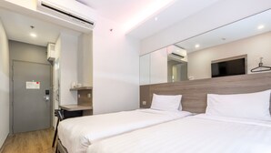 A hotel room with two beds, a wooden headboard, a large mirror, a TV, and a small table with a cup and saucer.