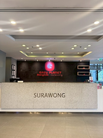A reception desk with a sign for Easy Planet Bangkok and Surawong, a tiled floor, and a ceiling with recessed lighting.