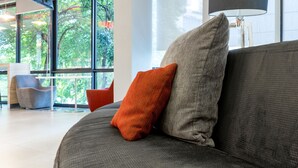 A modern living room with a grey sofa, a red cushion, and a large window offering a view of trees.