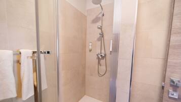 A glass-enclosed shower stall with beige tiles, a handheld showerhead, and a wall-mounted faucet.
