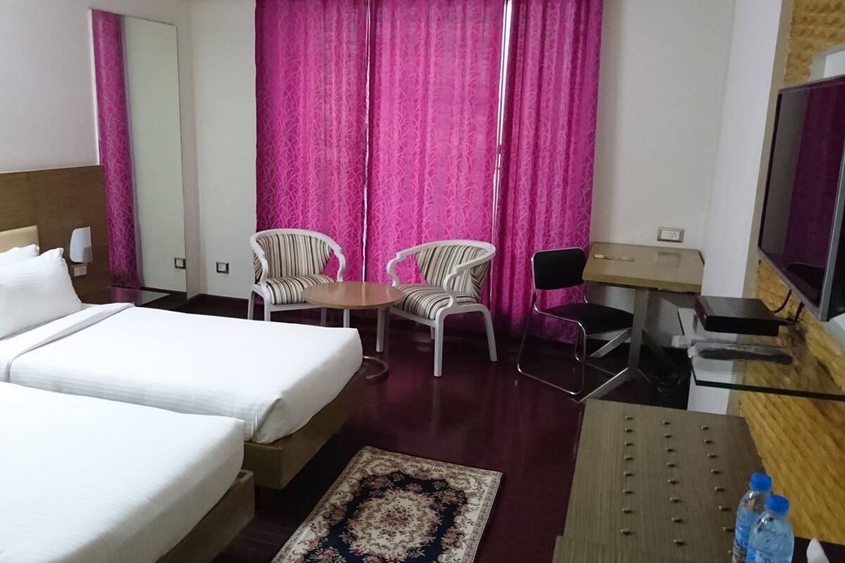 A hotel room with two beds, a desk, a chair, a television, and a small table.