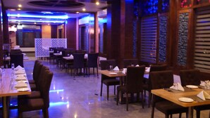 Een restaurant met meerdere tafels en stoelen, een betegelde vloer en een blauw verlicht plafond.