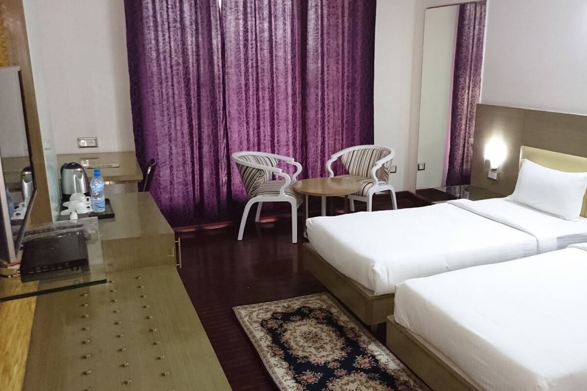A hotel room with two beds, a small table, two chairs, a coffee maker, and a water bottle on a counter.