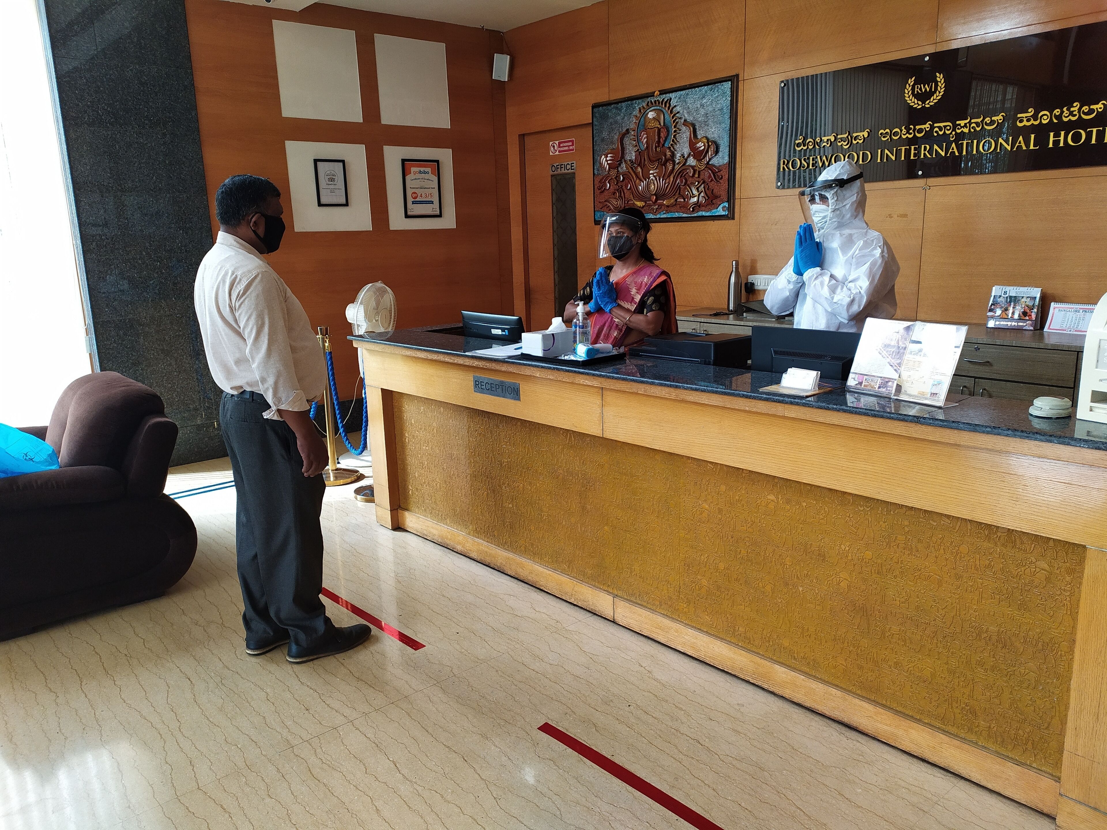 A hotel reception area with a wooden reception desk, a framed certificate, and a sign for Rosewood International Hotel.