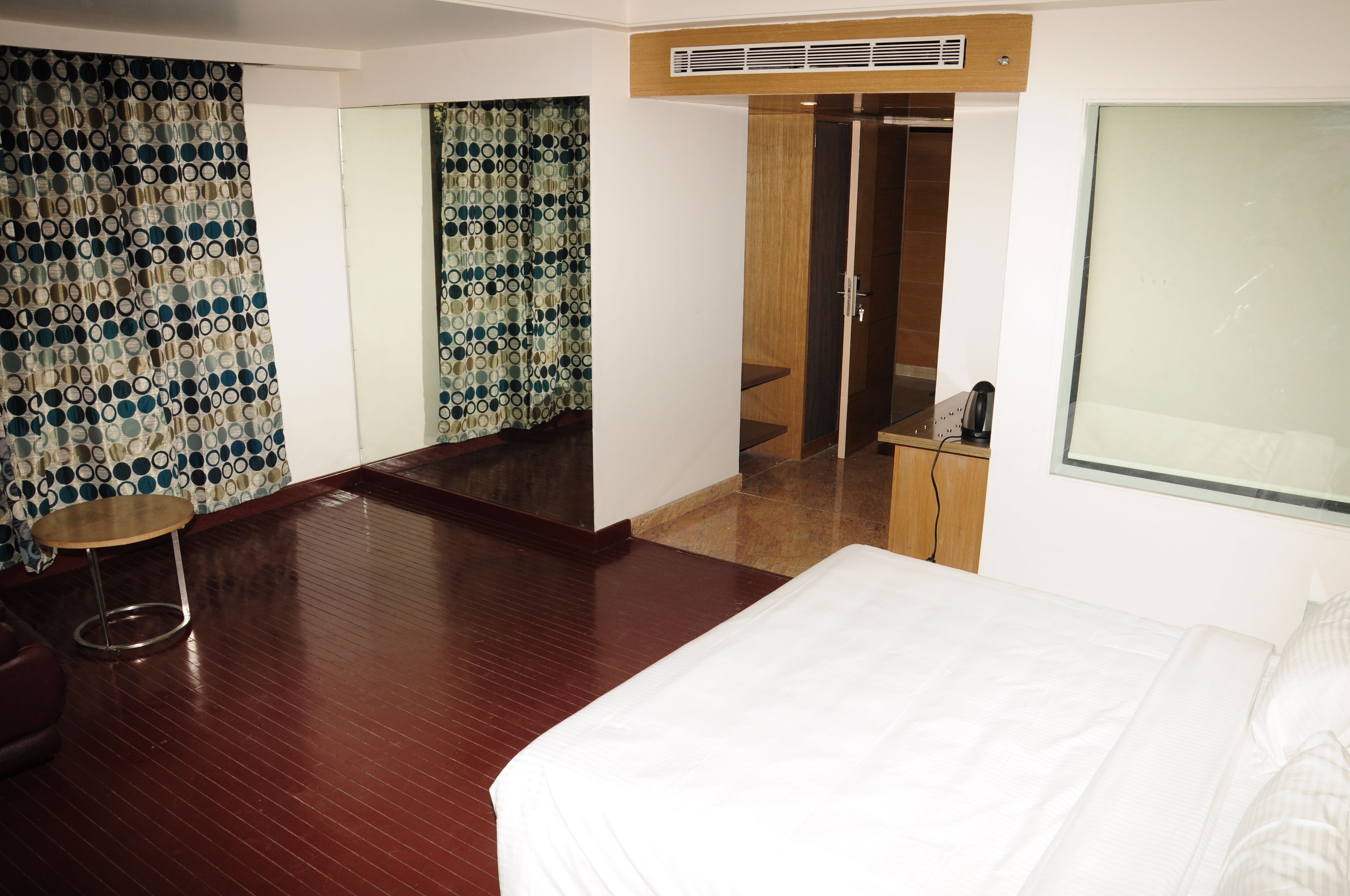 A hotel room with a bed, a round table, a mirror, and a wardrobe.