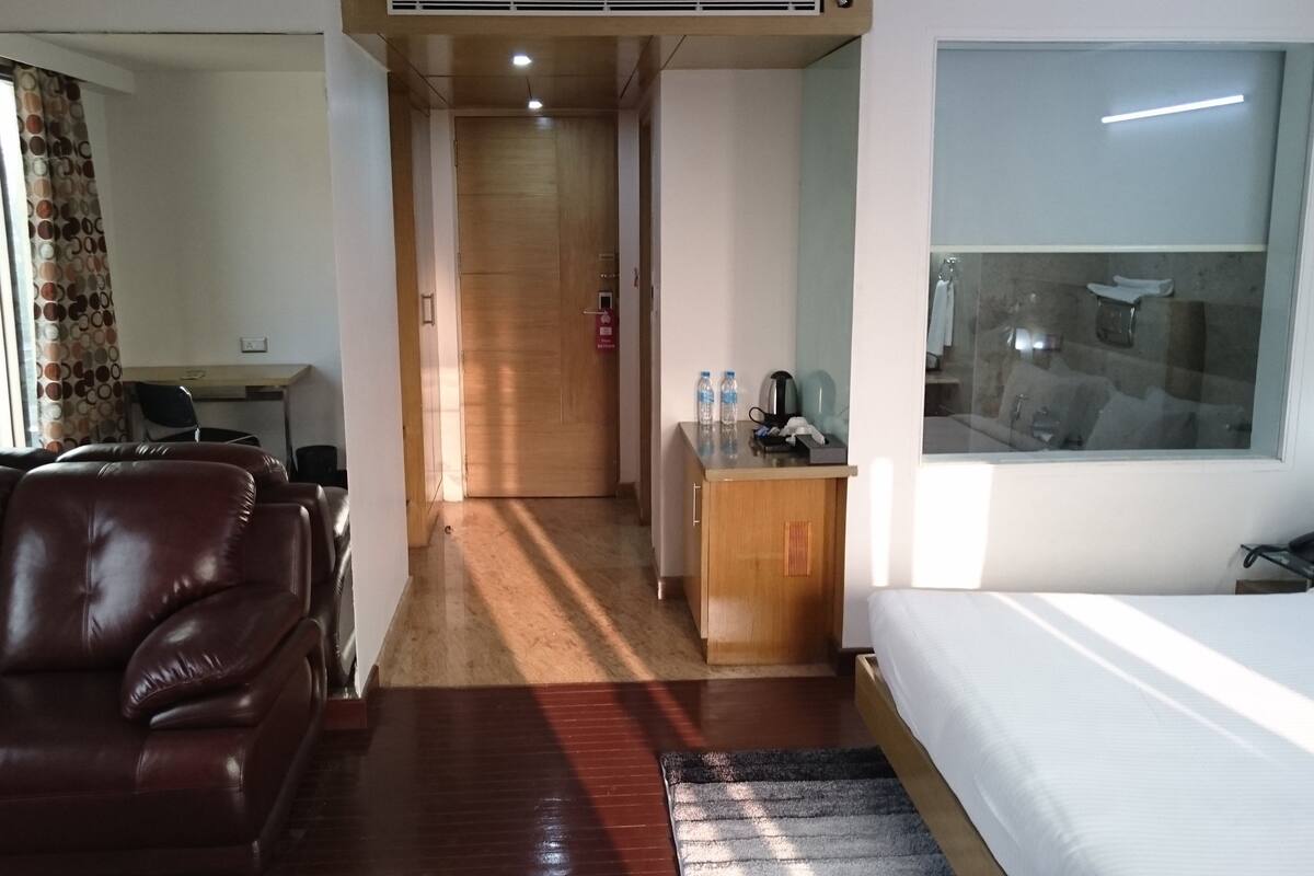 A hotel room with a leather sofa, a bed, a desk with a chair, and a small kitchenette area.