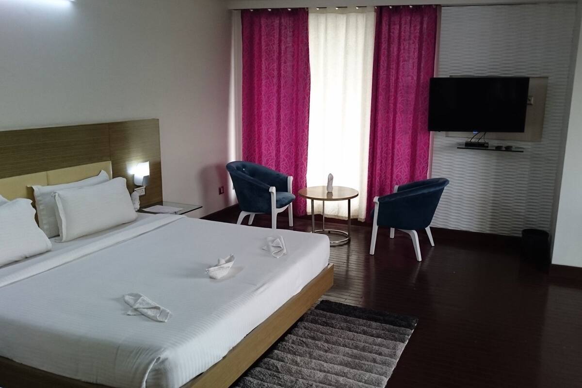 A hotel room with a bed, two chairs, a small table, a TV, and a window with curtains.