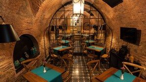 Un restaurante con un interior rústico de piedra, mesas de madera con manteles azul turquesa y un suelo de baldosas.