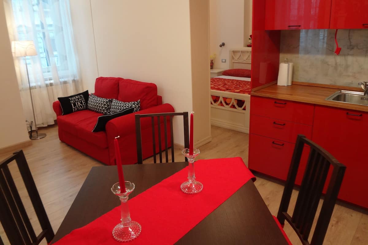 Un espacio habitable compacto con un sofá rojo, una mesa de comedor con dos velas y una zona de cocina con armarios rojos.