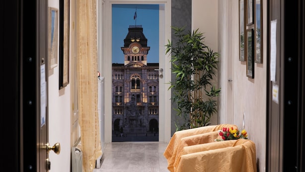A hallway with a view of a historic building, a radiator, a plant, and a table with a yellow tablecloth. - Rooms Boutique Carducci (Trieste)