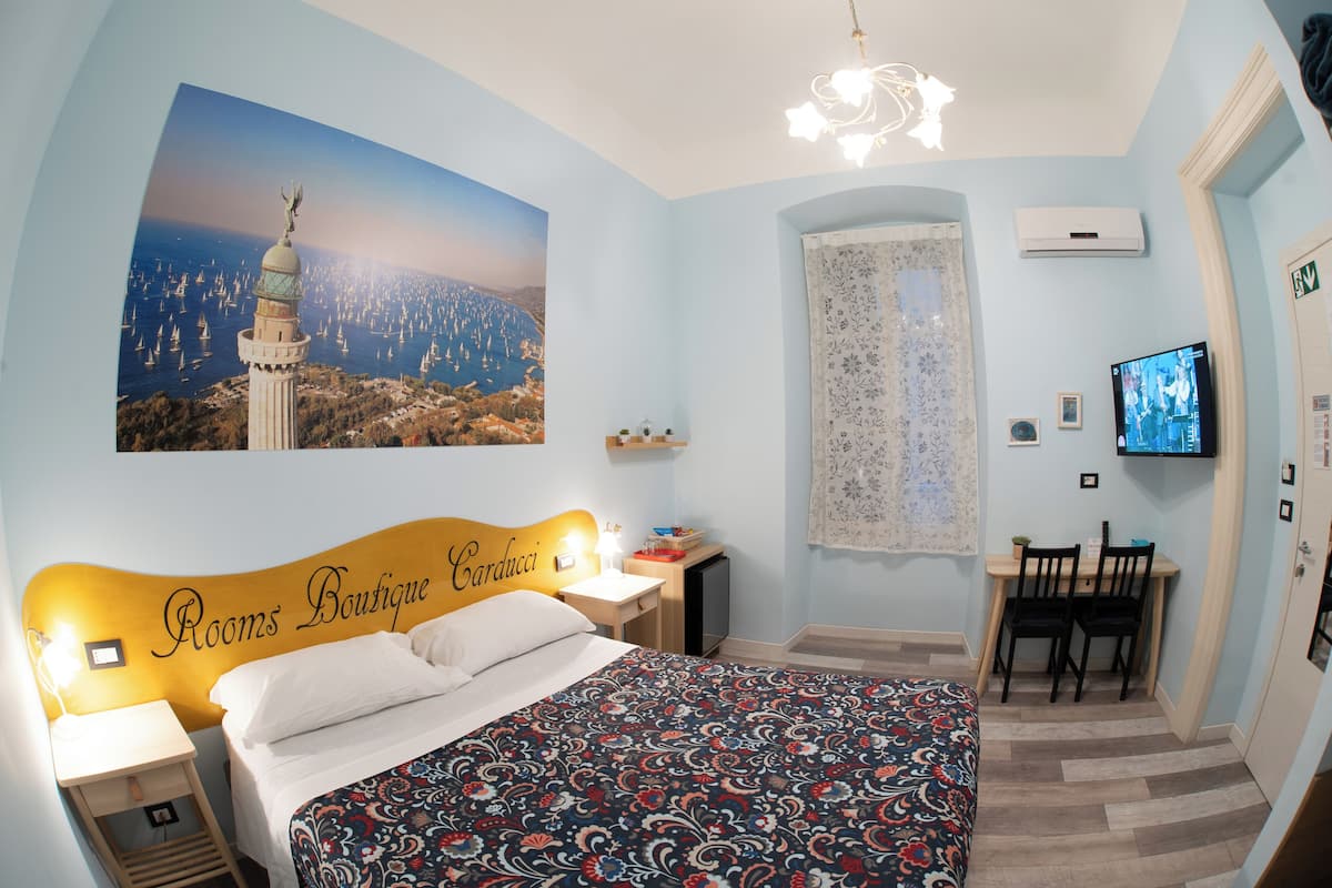 Habitación de hotel con cama, escritorio, televisor y ventana grande con vista al mar.