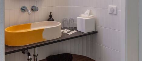 A bathroom with a white tiled wall, a yellow sink, a mirror with LED lights, a wooden shelf, and a hanging towel.