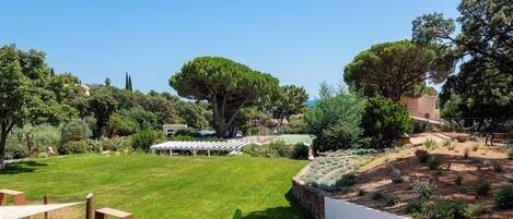 A well-maintained garden with a lawn, trees, and a white wall with a tiled roof structure.