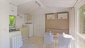 Una cocina compacta con estufa, microondas y armarios, una mesa de comedor con sillas y una ventana con cortinas.