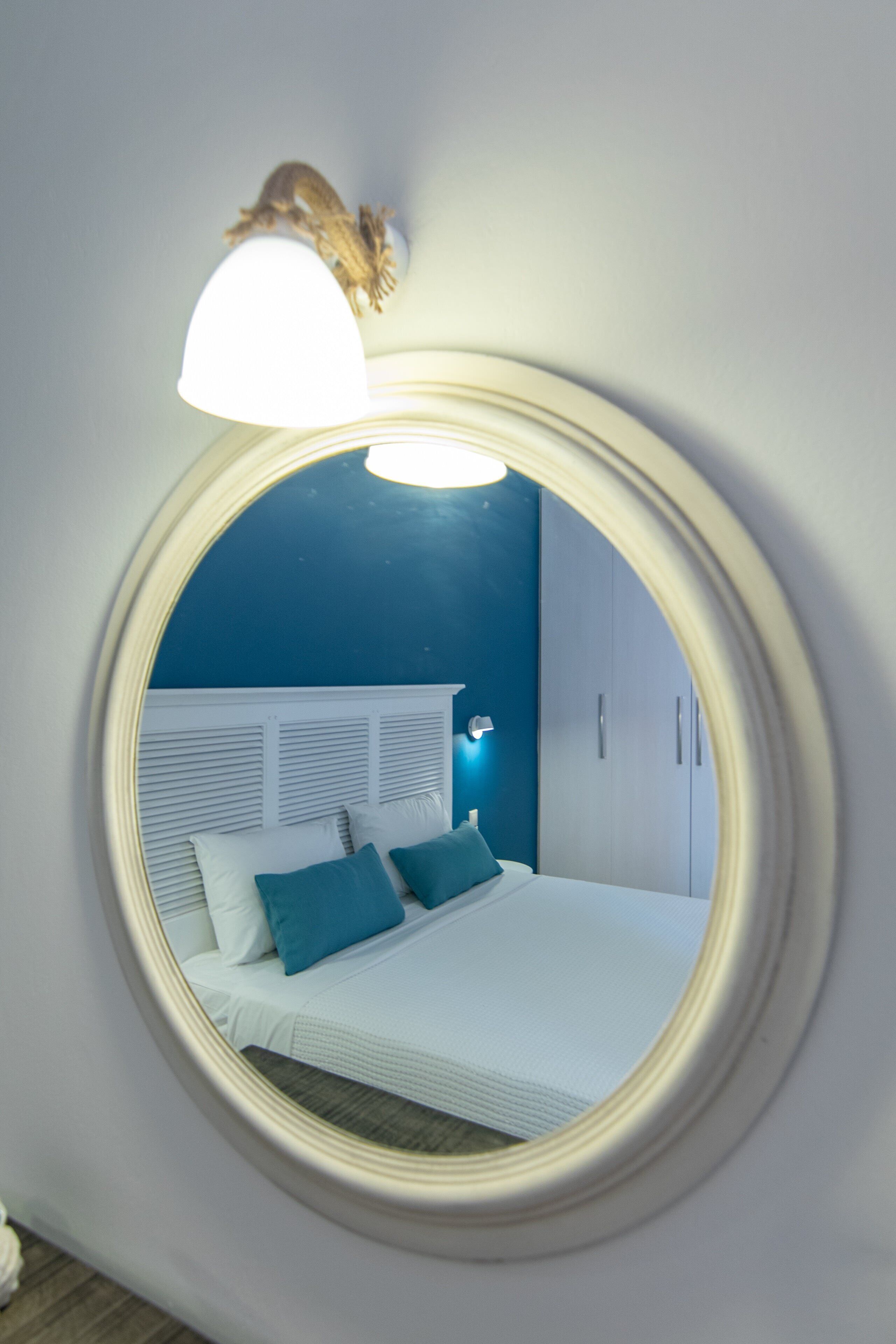 Ein runder Spiegel, der ein Schlafzimmer mit Bett, Kissen und Nachttisch reflektiert.