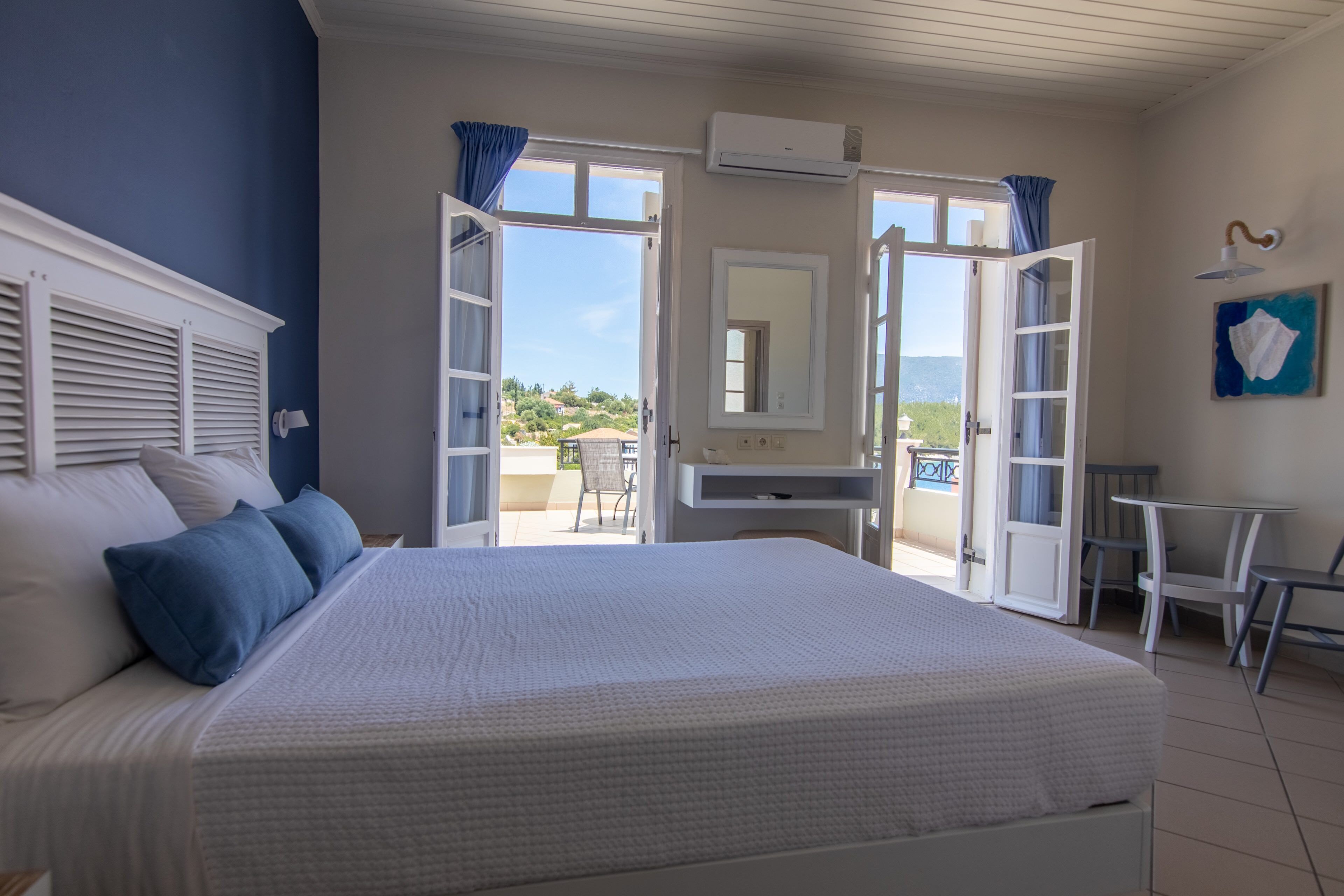 A bedroom with a large bed, a desk, and an open door leading to a balcony.