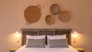 A neatly made bed with two pillows, a headboard, and wall-mounted woven baskets. - Fiscardo Studios (Kefalonia)