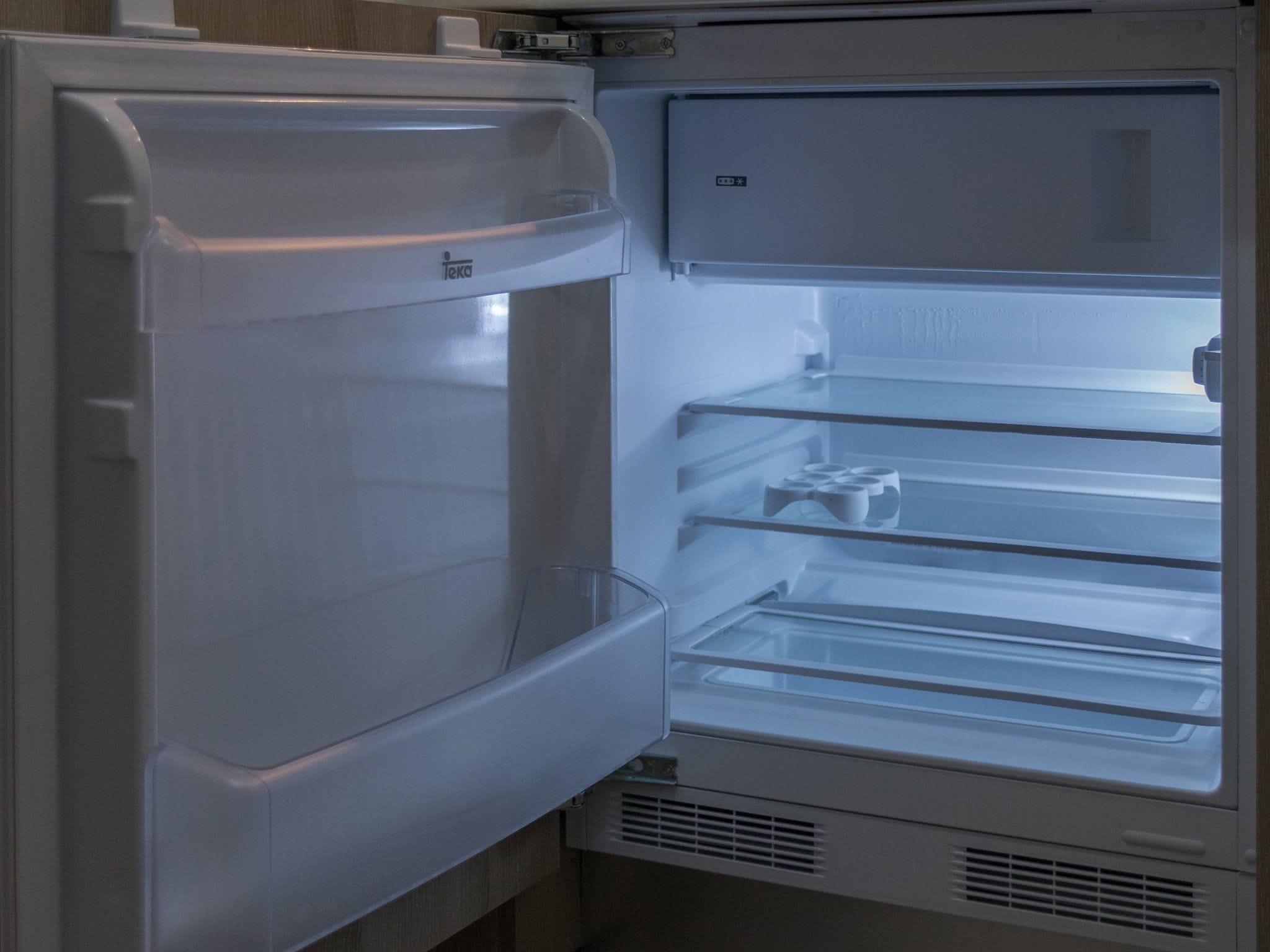 Geladeira aberta com várias prateleiras e compartimento congelador.