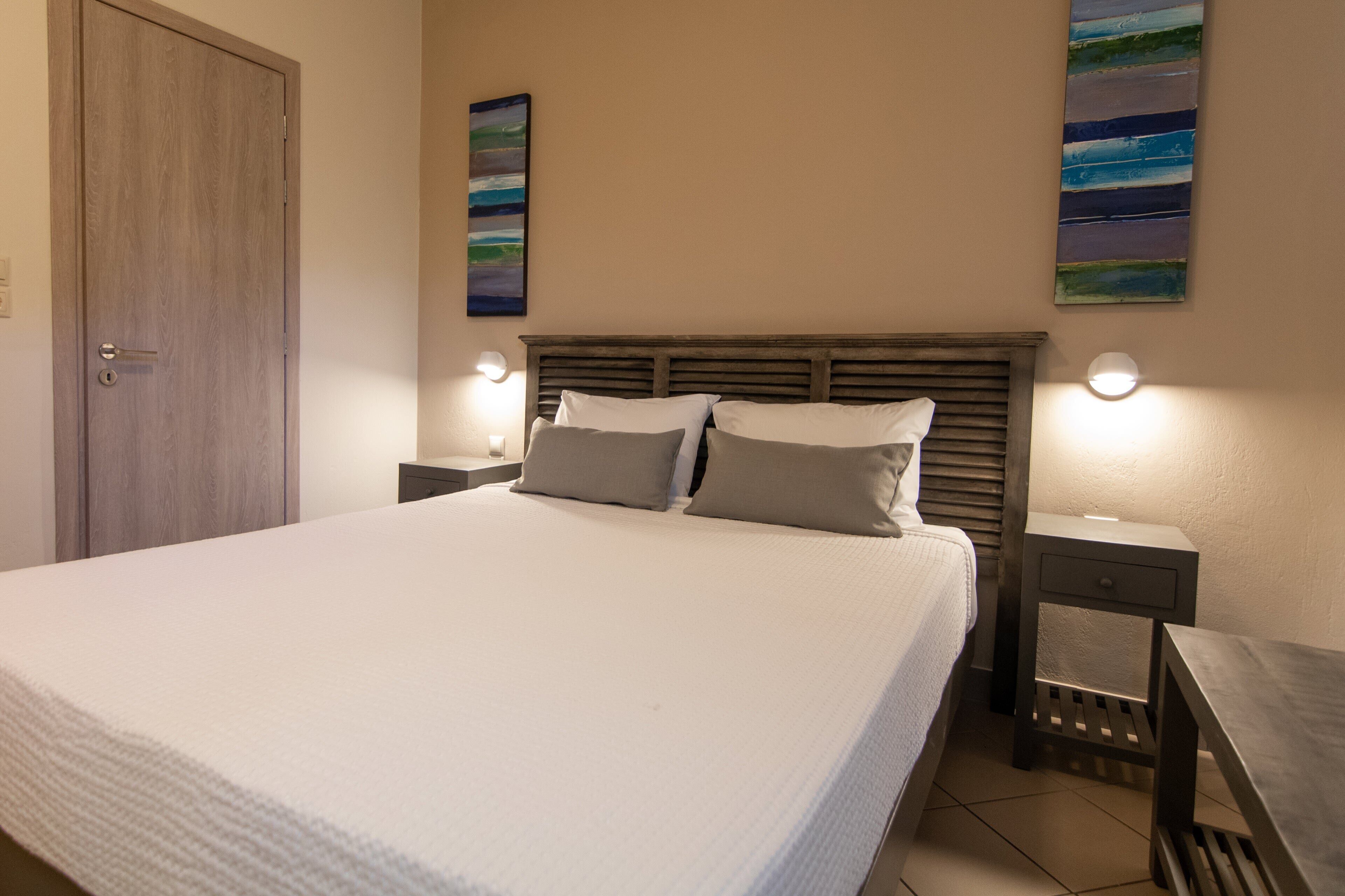 A neatly made bed with a wooden headboard, two bedside tables with lamps, and two abstract paintings on the wall.
