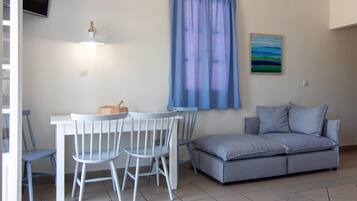 A room with a white table and chairs, a grey sofa, a blue curtain, and a painting on the wall.
