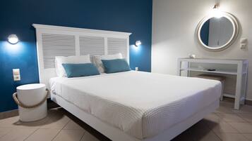 Un dormitorio con cama blanca, almohadas azules, un espejo redondo sobre un tocador blanco y una pared azul.