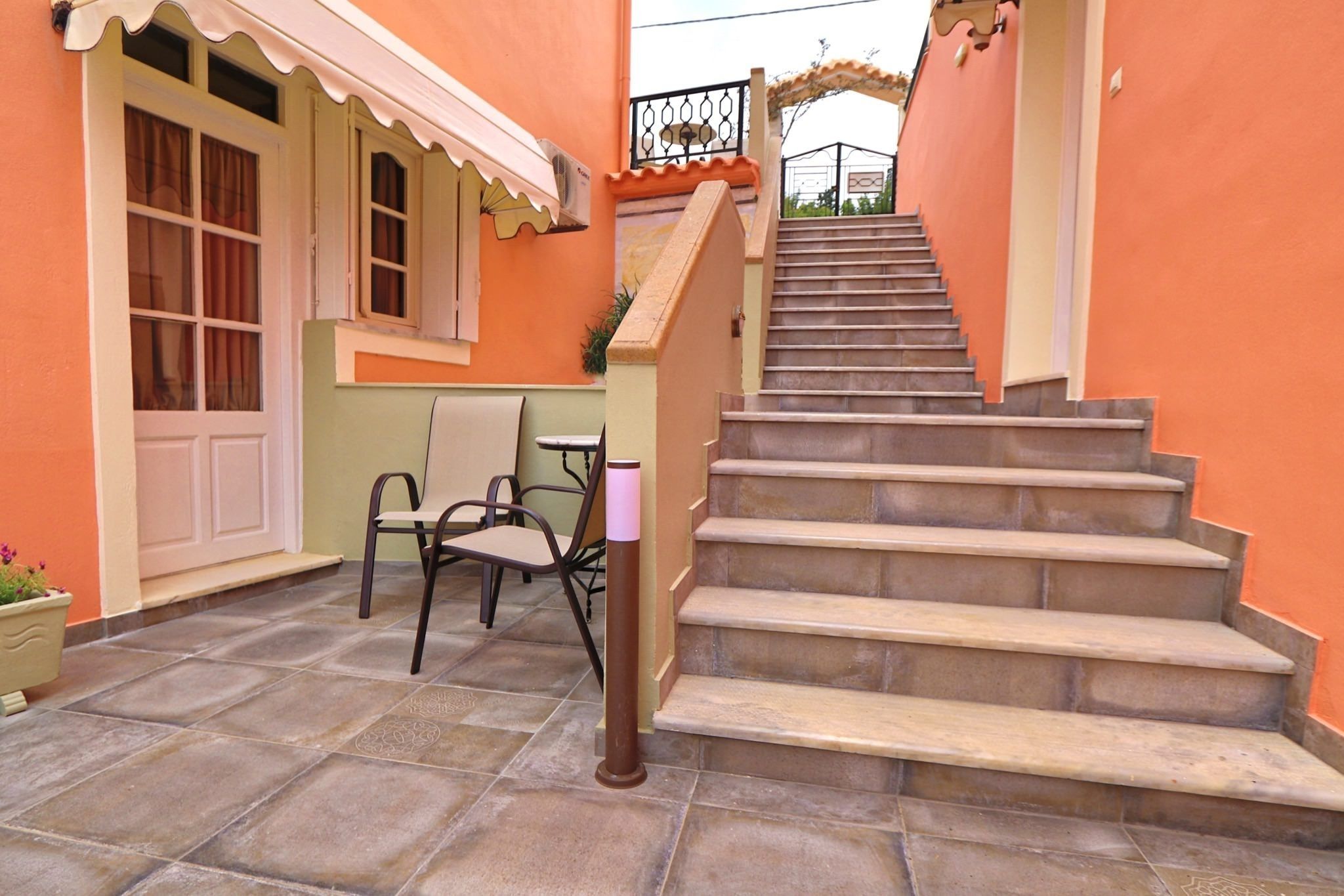 Eine Treppe führt zu einer Tür, einem Stuhl und einem Tisch in einem Innenhof mit orangefarbenen Wänden.