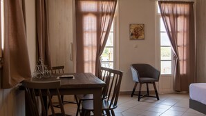 A room with a wooden table, chairs, a bed, and curtains. - Fiscardo Studios (Kefalonia)