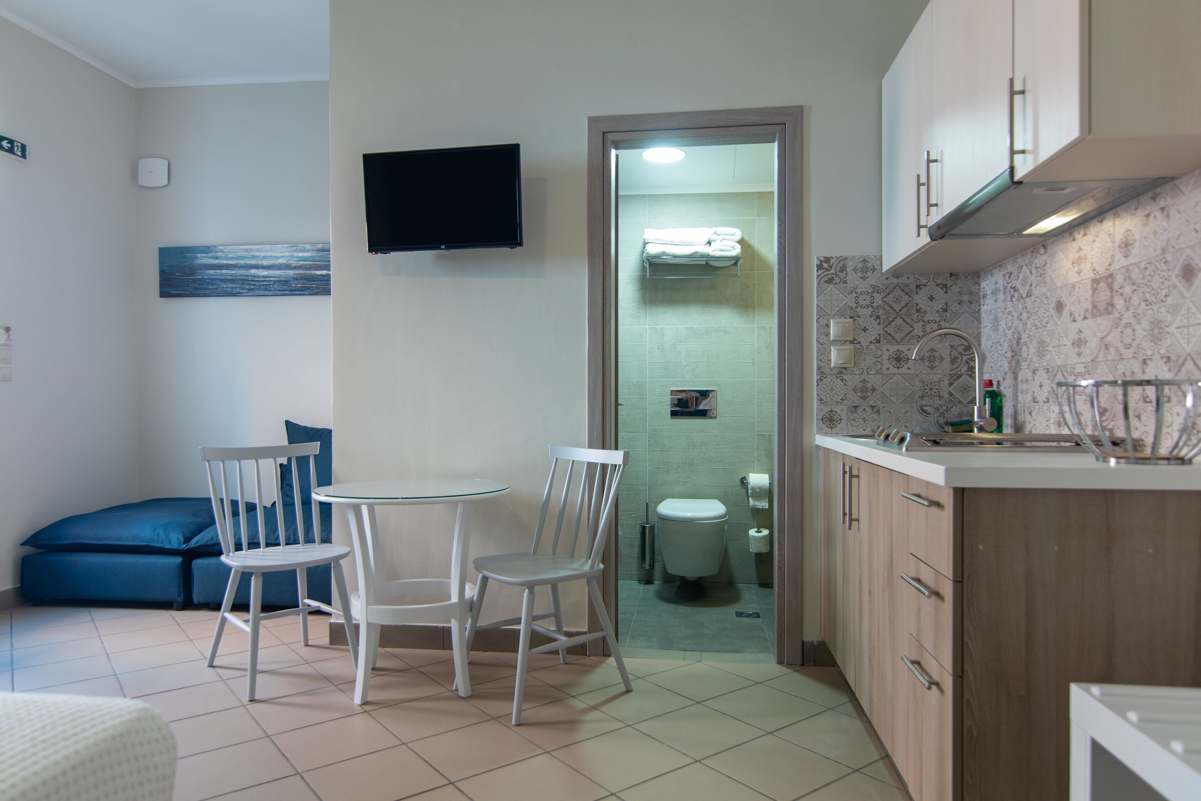 Une cuisine compacte avec un coin repas, un téléviseur et une salle de bain visible à travers une porte ouverte.