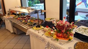 A buffet with various dishes and a centerpiece of flowers. - Hotel Vienna (San Mauro Pascoli)