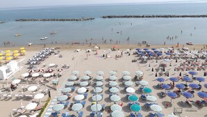 A beach with numerous umbrellas and sun loungers, a rocky breakwater, and calm waters. - Hotel Vienna (San Mauro Pascoli)