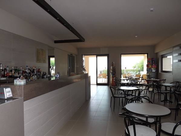 A bar area with a tiled counter, multiple seating tables, and chairs. - Hotel Vienna (San Mauro Pascoli)