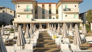 A hotel with multiple floors, outdoor seating area with umbrellas, and a sandy ground. - Hotel Vienna (San Mauro Pascoli)