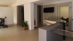 A modern hotel lobby with a reception desk, a potted plant, and a stroller. - Hotel Vienna (San Mauro Pascoli)