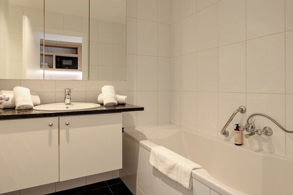 A modern bathroom with a sink, mirror, and bathtub. - Diamant Suites Brussels EU (Brussels)
