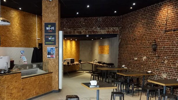 A cafe with a rustic brick wall, wooden counter, and multiple tables and chairs. - Urban City Centre Hostel (Brussels)