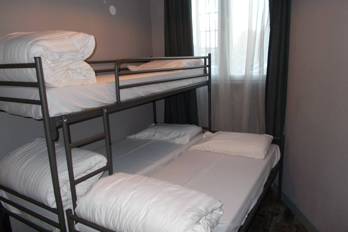 A bunk bed room with white bedding and a window with curtains.