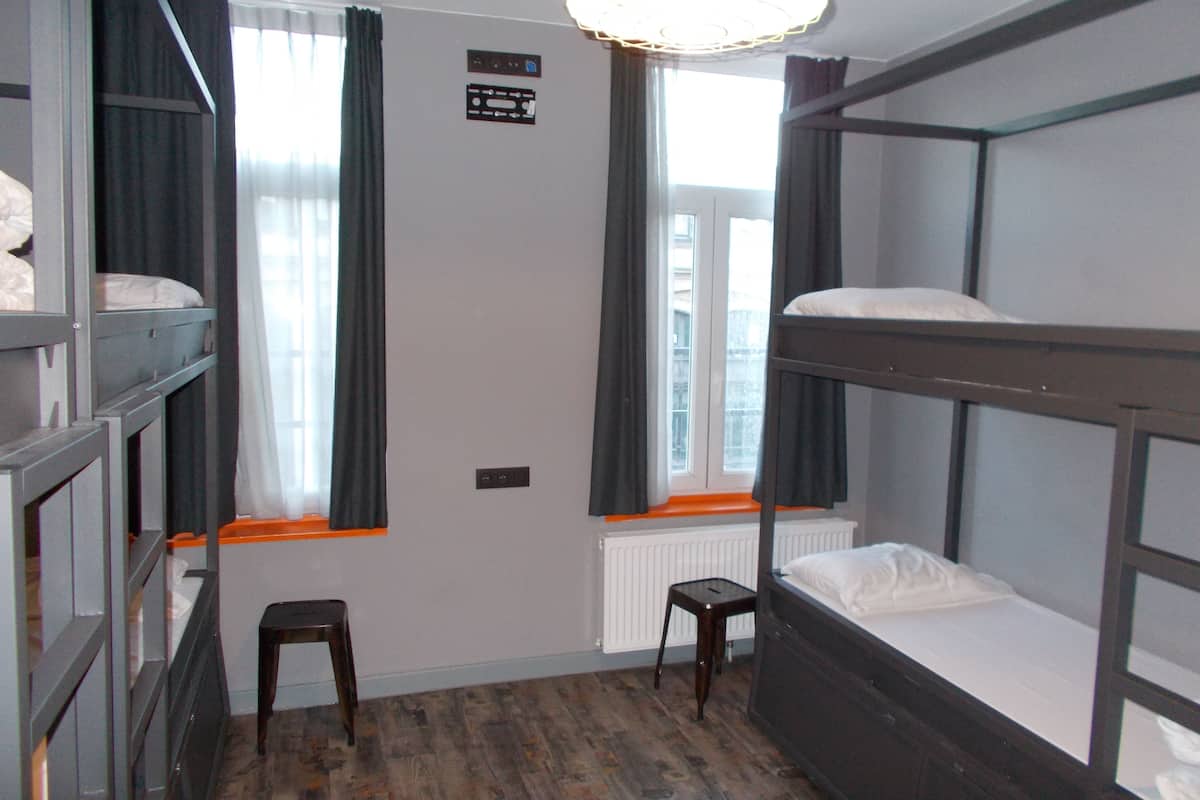 A bunk room with two bunk beds, a small stool, a window with curtains, and a light fixture.