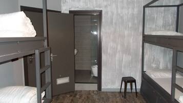 Un dormitorio con literas, un taburete pequeño y una puerta que da a un baño.
