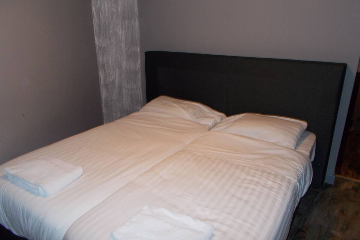 A bed with a dark headboard and white linens, including two folded towels.