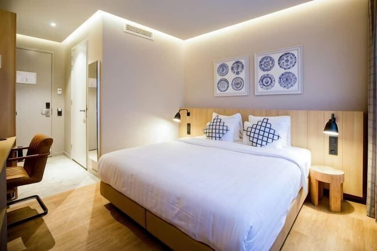A modern hotel room with a large bed, a desk, and a chair.