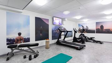 Un gimnasio con cintas de correr, una banca y mancuernas.