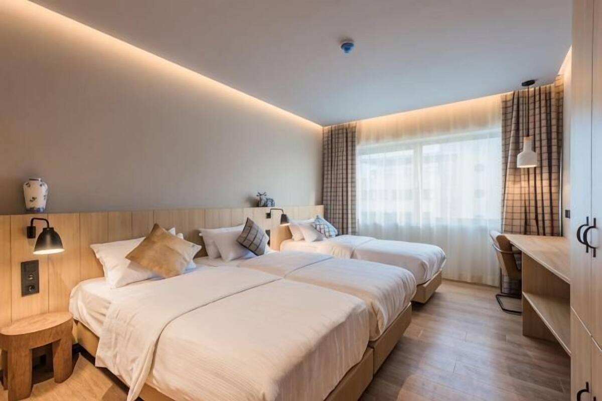A hotel room with two beds, a desk, a lamp, and a window with curtains.