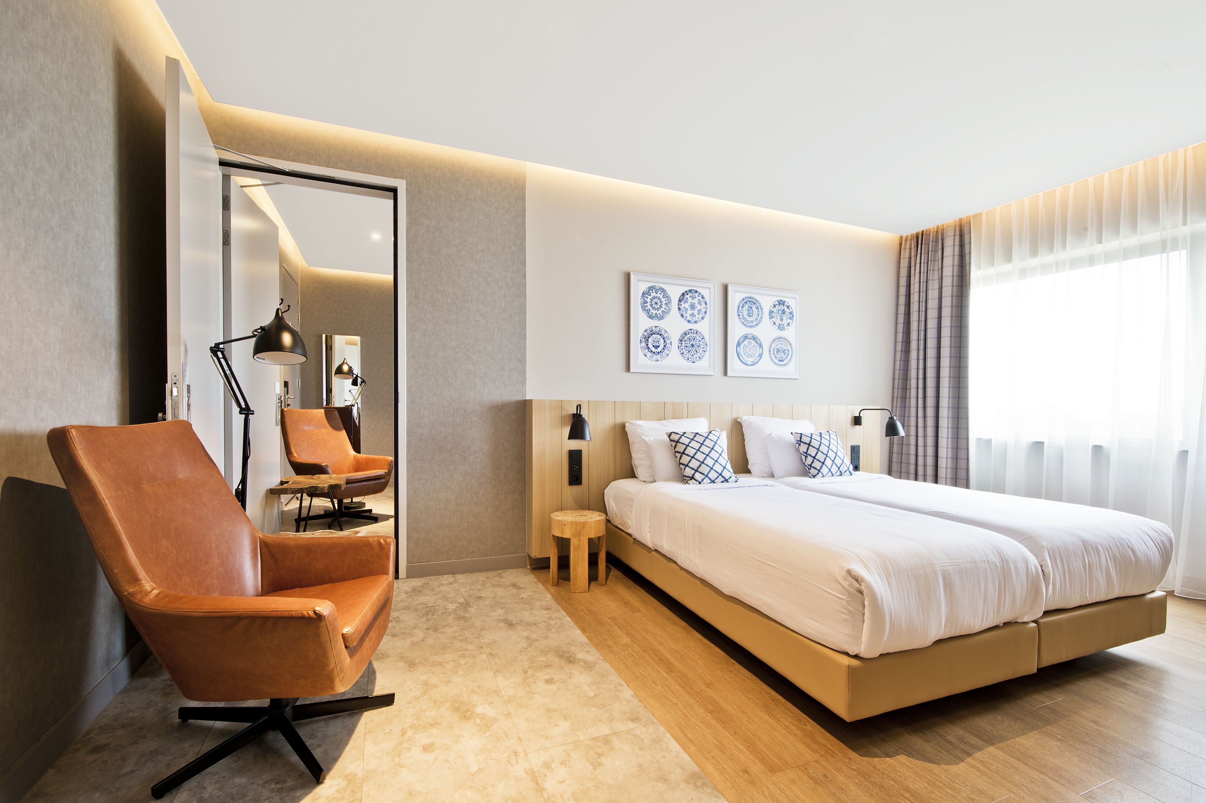 A modern hotel room with a large bed, a leather armchair, a small side table, and a mirror.