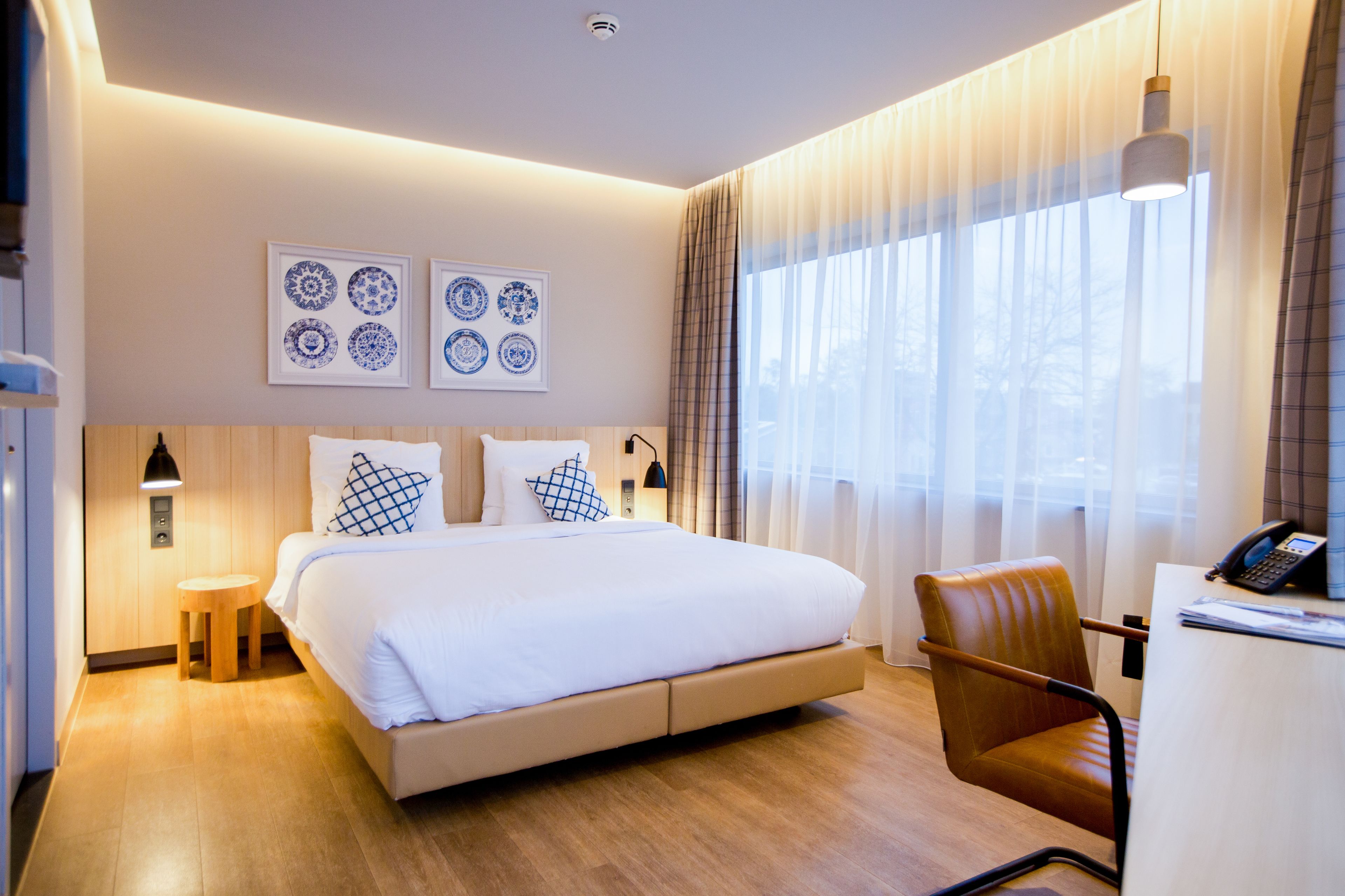 A modern hotel room with a large bed, a desk with a telephone, and a chair.